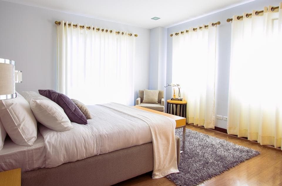 A bright bedroom with a neatly made bed, light curtains and clear floor space